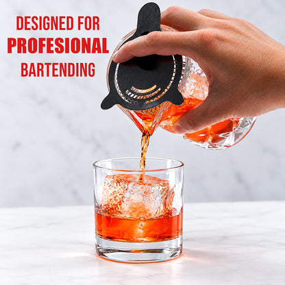 Pouring a stirred cocktail from the mixing glass through a julep strainer into a rocks glass